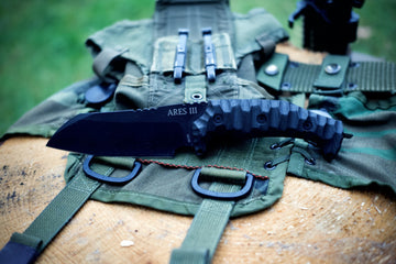 Detailní pohled na lovecký nůž ARES III položený na zelené taktické vestě