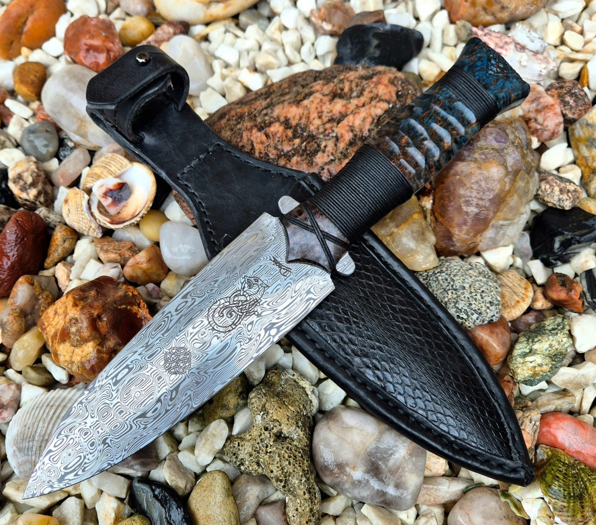Detailní pohled na luxusní dýku z nerezové damaškové oceli s koženým pouzdrem z hadí kůže položenou na mořských kamenech