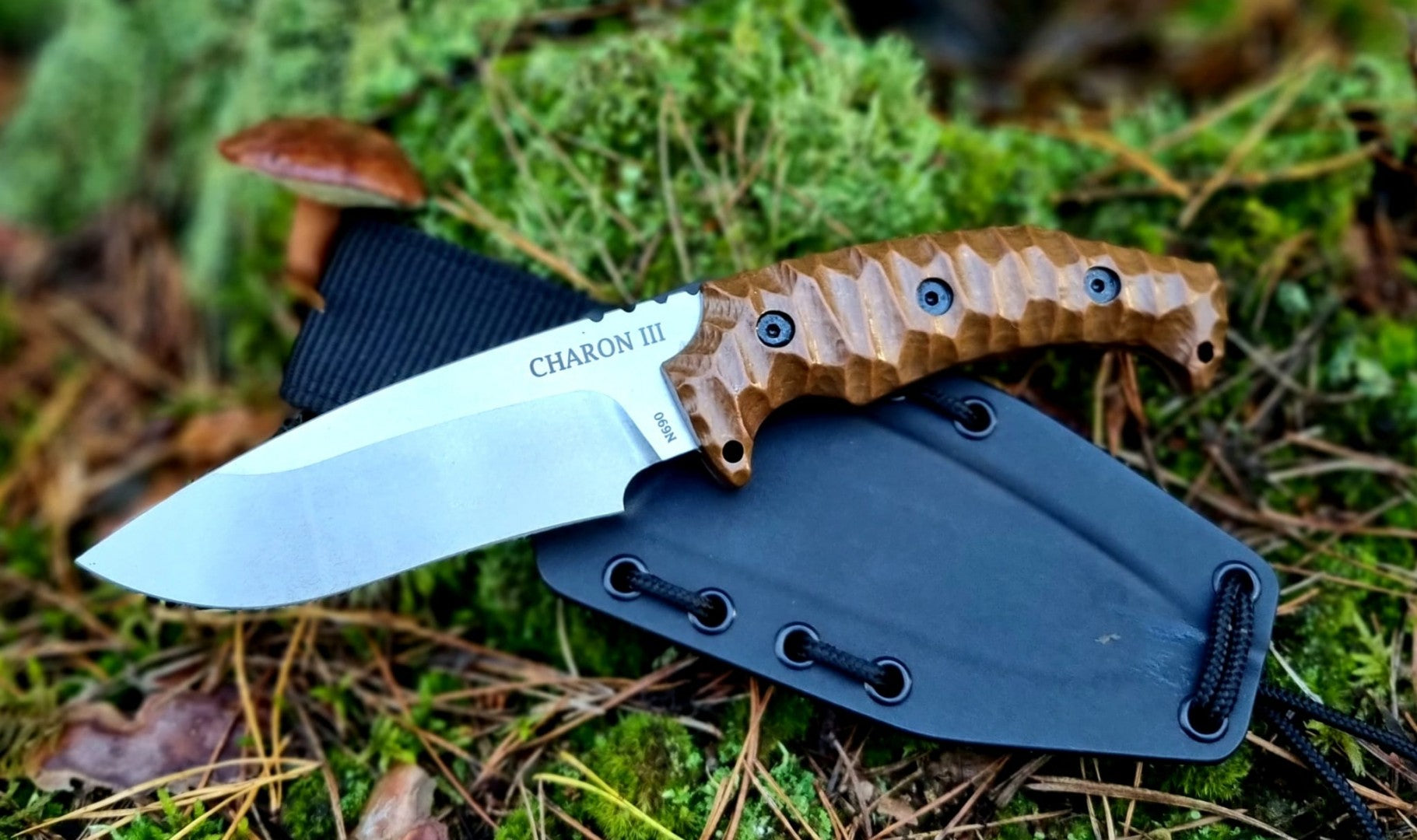 Lovecký nůž Charon III, stonewash položený na kydexovém pouzdře mezi listím 